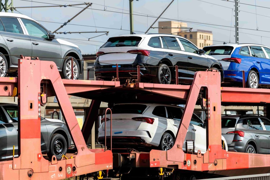 Several new cars are loaded onto a red double-decker train car transporter, with power lines and buildings visible in the background—a scene reminiscent of the efficiency and reliability offered by FL Auto Transport Tallahassee.